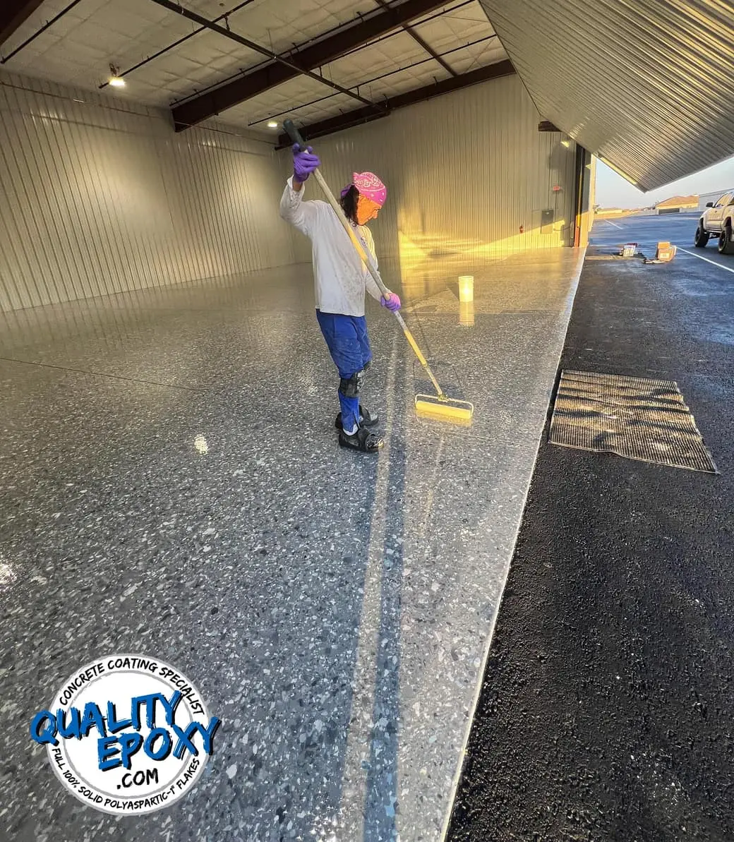 Rolling the polyaspartic top coat across a flake floor inside an aircraft hangar at sunset