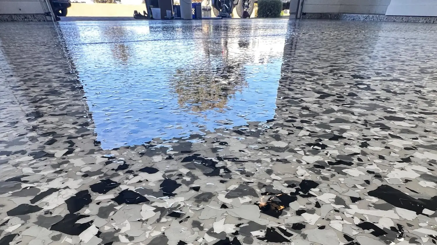 A Tuxedo one-inch flake garage floor in black, white and grey, with the open garage door and a palm tree reflected in its top coat